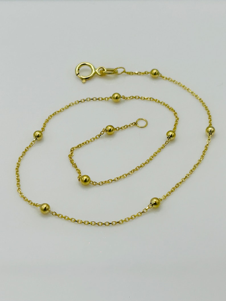 May include: A gold chain anklet with small round beads. The anklet has a lobster clasp closure.