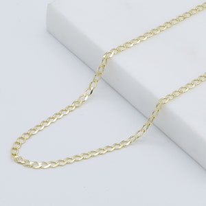 May include: A gold chain necklace with a curb link style. The chain is laying flat on a white surface.