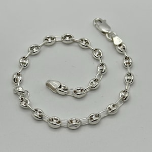 May include: A silver-colored bracelet with a series of connected, rounded links. The bracelet features a lobster clasp closure. The links are smooth and shiny, reflecting light. The bracelet is designed to be worn around the wrist.