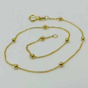 May include: A gold chain anklet with small round beads. The anklet has a lobster clasp closure.