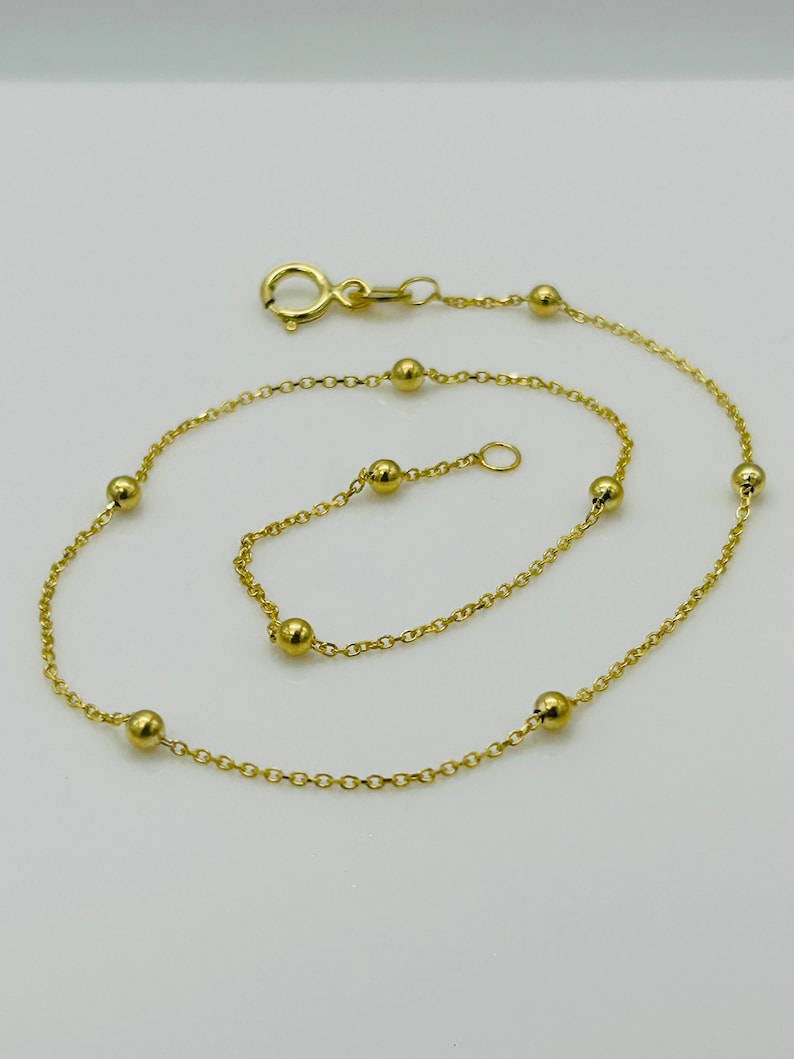 May include: A gold chain anklet with small round beads. The anklet has a lobster clasp closure.