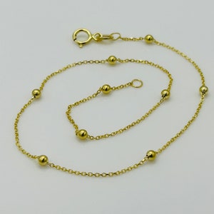 May include: A gold chain anklet with small round beads. The anklet has a lobster clasp closure.