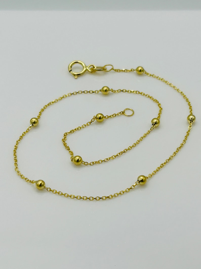 May include: A gold chain anklet with small round beads. The anklet has a lobster clasp closure.