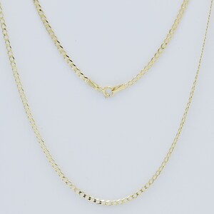 May include: A gold chain necklace with a curb link style. The chain is shown laying flat on a white surface.