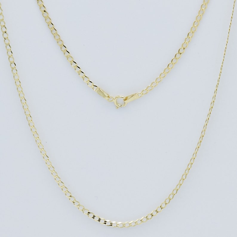 May include: A gold chain necklace with a curb link style. The chain is shown laying flat on a white surface.