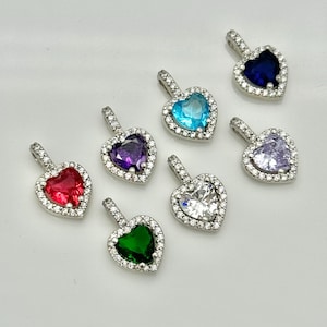 Può includere: Sette ciondoli a forma di cuore in argento con pietre preziose di diversi colori. I ciondoli hanno un'aureola di pietre più piccole e chiare intorno alla pietra centrale. I colori delle pietre sono rosso, verde, viola, blu, azzurro, trasparente e rosa.