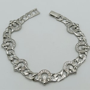 Könnte beinhalten: Ein silbernes Armband mit einem Gliederketten-Design und einem sich wiederholenden Muster aus einem stilisierten Distel mit einer Krone oben. Jede Distel ist von klaren Strasssteinen umgeben.