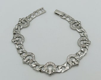 May include: A silver bracelet with a chain link design and a repeating pattern of a stylized thistle with a crown on top. Each thistle is surrounded by clear rhinestones.