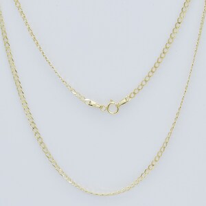 May include: A gold chain necklace with a lobster clasp closure. The chain is a curb style with a flat, slightly rounded design.