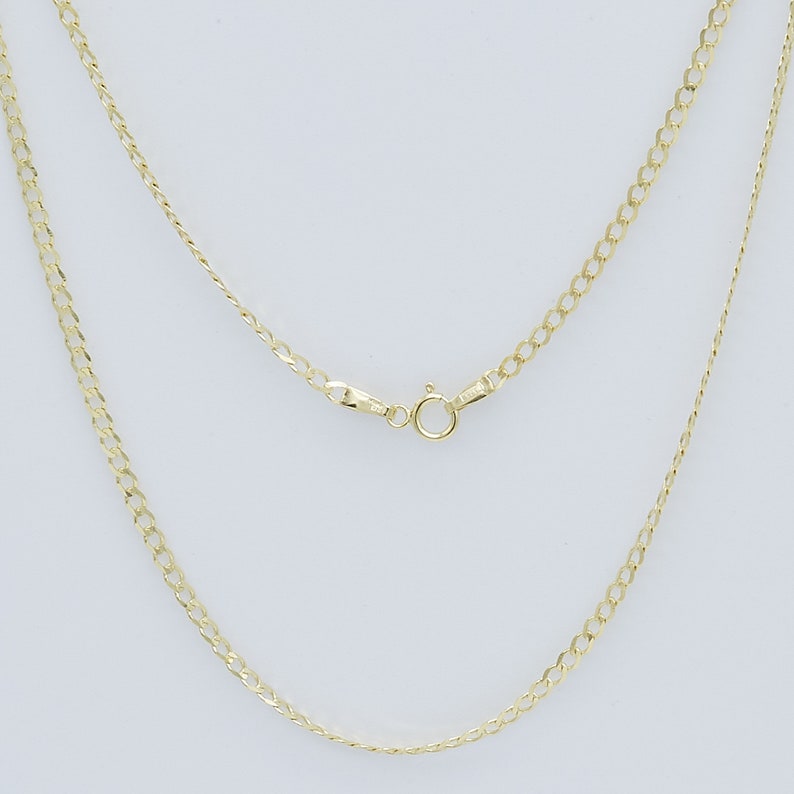 May include: A gold chain necklace with a lobster clasp closure. The chain is a curb style with a flat, slightly rounded design.