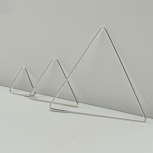 Könnte beinhalten: Drei silberfarbene, dreieckige Ausstecher in verschiedenen Größen sind zu sehen. Die Ausstecher bestehen aus dünnem Metalldraht mit einem einfachen, geometrischen Design. Der größte Ausstecher ist etwa 10 cm breit.