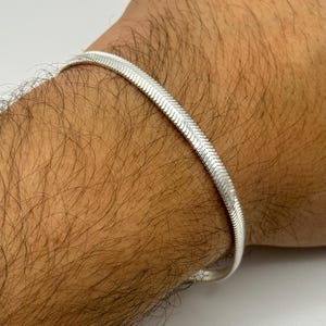 Puede incluir: Un brazalete de cadena de serpiente de plata en la muñeca de una persona.