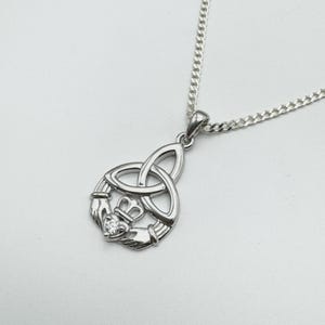 May include: A silver Claddagh pendant necklace. The pendant features a heart, crown, and hands design, with a small, clear gemstone at the centre. The necklace has a curb chain.