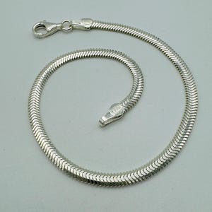 May include: A silver snake chain bracelet with a lobster clasp. The bracelet is made of small, interlocking metal pieces, creating a smooth, flexible design. The bracelet is shown against a light grey background.