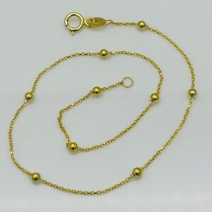 May include: A gold chain anklet with small round beads. The anklet has a lobster clasp closure.