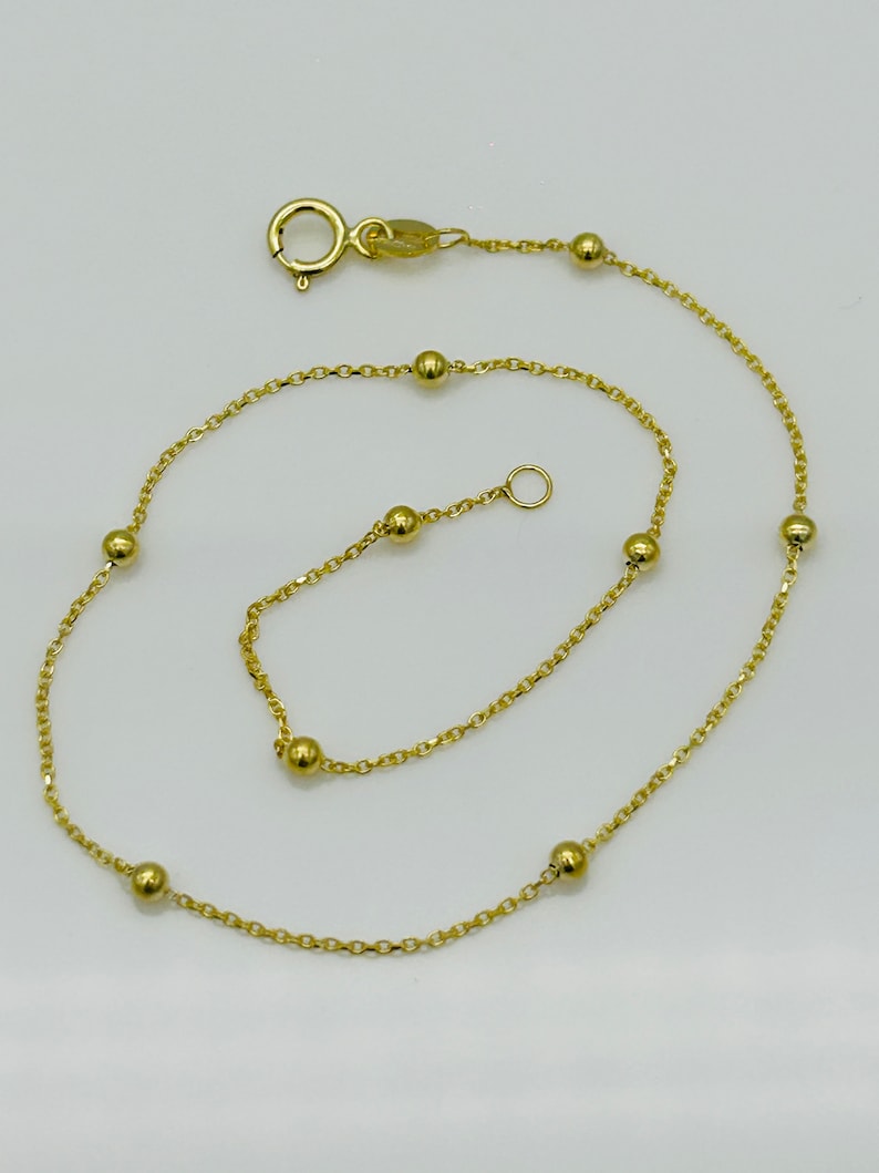 May include: A gold chain anklet with small round beads. The anklet has a lobster clasp closure.