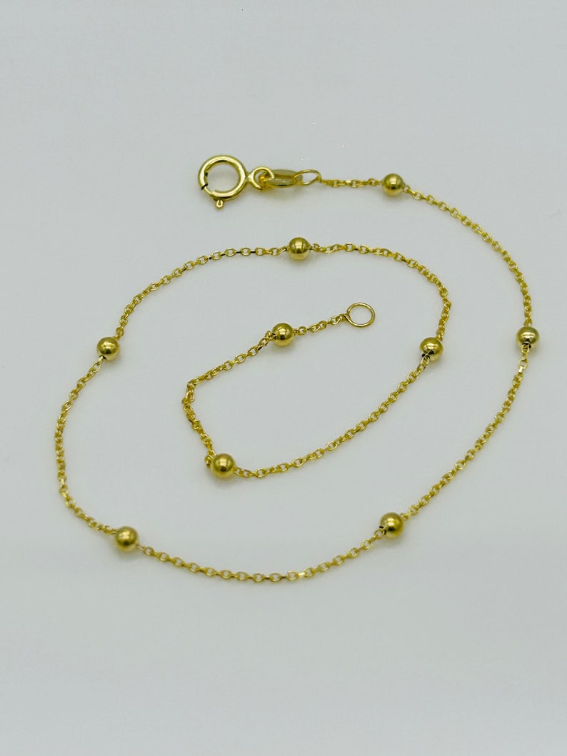 May include: A gold chain anklet with small round beads. The anklet has a lobster clasp closure.