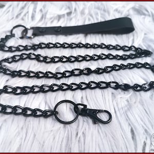 May include: A black chain leash with a handle and a clasp. The chain is made of interlocking links and is designed for attaching to a collar or harness. The handle is a black strap.