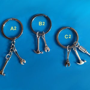 May include: Three silver keyrings with different tool charms. The first keyring has a hammer and wrench charm, the second has a hammer and wrench charm, and the third has a hammer, wrench, and screwdriver charm. The keyrings are labelled A2, B2, and C2.