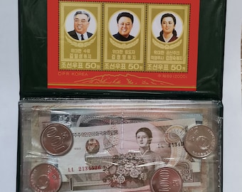 May include: A black leather folder with a clear plastic window. The window displays three stamps featuring portraits of Kim Il-sung, Kim Jong-il, and Kim Jong-suk. The stamps are from the Democratic People's Republic of Korea (DPRK) and commemorate the 55th anniversary of the founding of the Workers' Party of Korea. The folder also contains a North Korean banknote and several North Korean coins.