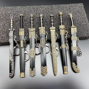 Peut inclure: Une collection de sept épées miniatures, chacune avec un design unique. Les épées présentent des détails complexes dans des tons argent et bronze, avec des lames noires. Chaque épée est attachée à un porte-clés.
