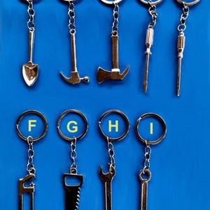 May include: Nine silver keychains with different tool charms. The charms include a shovel, hammer, axe, screwdriver, saw, and wrenches. The keychains are labelled with letters A through I.