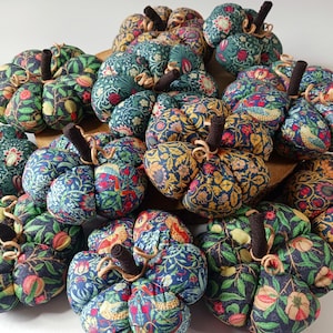 May include: A group of fabric pumpkins with dark brown stems and curly tendrils. The pumpkins are adorned with vibrant floral patterns in blue, green, red, and yellow. These autumn-themed decorations are perfect for the fall season.