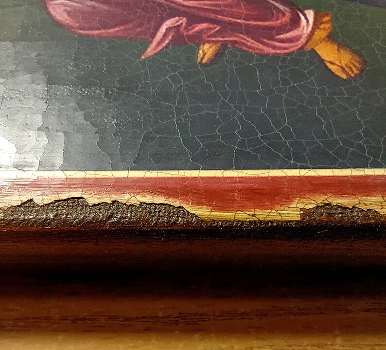May include: Close-up of the bottom edge of a framed painting. The frame is made of dark wood with a red and gold trim. The paint on the frame is chipped and cracked, showing the wood underneath.
