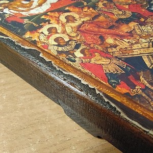 May include: A religious icon featuring a detailed painting with figures in red, gold, and white. The icon is set in a dark brown wooden frame with visible wear and tear, suggesting age and use. The artwork depicts a religious scene.