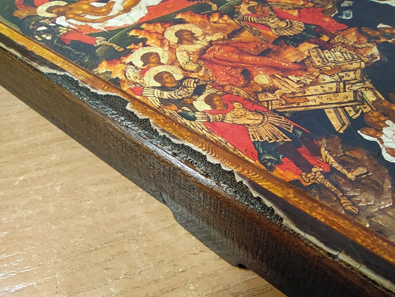 May include: A religious icon featuring a detailed painting with figures in red, gold, and white. The icon is set in a dark brown wooden frame with visible wear and tear, suggesting age and use. The artwork depicts a religious scene.