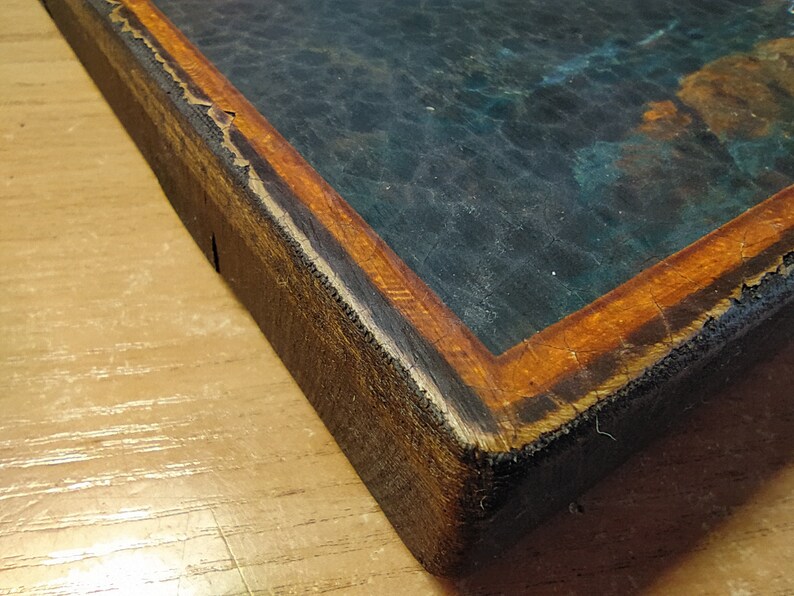 May include: Close-up of the corner of a wooden frame with a dark blue and green painting inside. The frame is made of dark wood with a thin orange border.