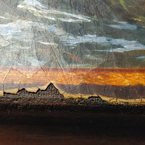May include: Close-up of a painting's bottom edge, showing a brown wooden frame with a layer of orange paint and a crackled surface.