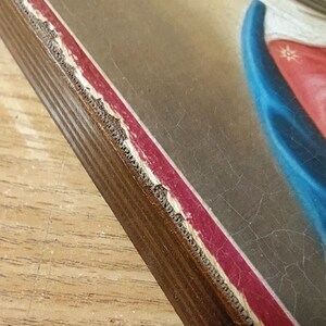 May include: A close-up of the edge of a wooden frame with a red and gold border. The frame is slightly chipped and worn, giving it a vintage look.