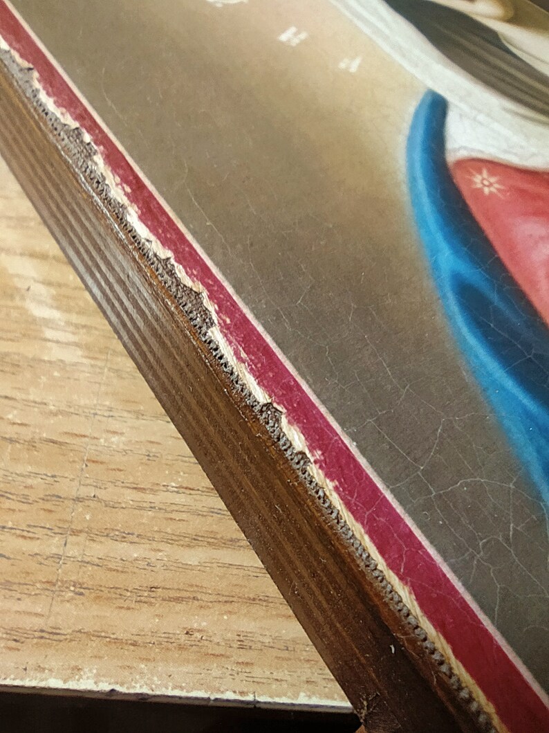 May include: A close-up of the edge of a wooden frame with a red and gold border. The frame is slightly chipped and worn, giving it a vintage look.