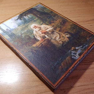 May include: A religious icon depicting a bearded man in a white robe kneeling in a forest setting. The icon is painted on a wooden panel with a brown frame. The text "The Holy Christian Faith" is visible in the upper right corner of the icon.