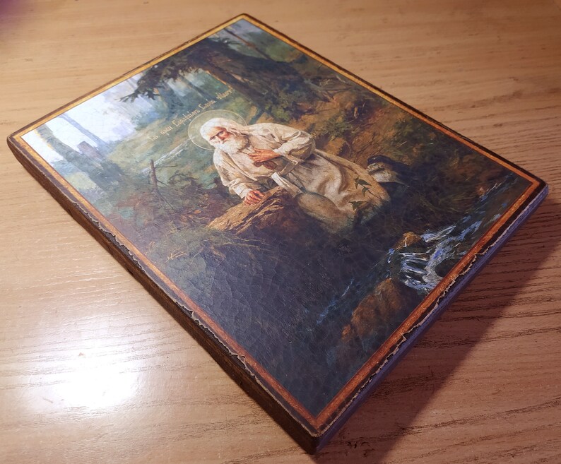 May include: A religious icon depicting a bearded man in a white robe kneeling in a forest setting. The icon is painted on a wooden panel with a brown frame. The text "The Holy Christian Faith" is visible in the upper right corner of the icon.