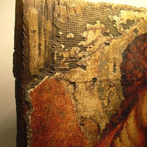 May include: Close-up of a weathered wooden panel with a faded painting of a person's face. The paint is cracked and peeling, revealing the wood underneath. The panel is likely part of an antique icon or religious artwork.