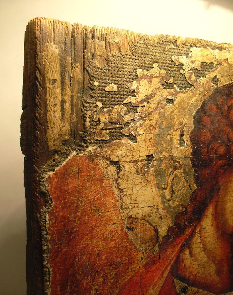 May include: Close-up of a weathered wooden panel with a faded painting of a person's face. The paint is cracked and peeling, revealing the wood underneath. The panel is likely part of an antique icon or religious artwork.