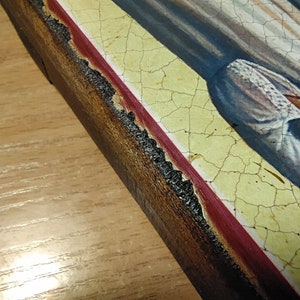 May include: A close-up of a wooden frame with a red and yellow border. The frame is cracked and worn, and the paint is peeling in places.