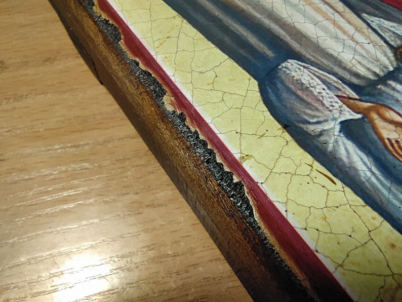 May include: A close-up of a wooden frame with a red and yellow border. The frame is cracked and worn, and the paint is peeling in places.