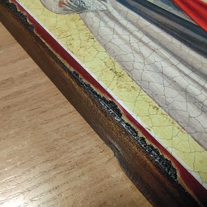 May include: Close-up of the edge of a wooden frame with a red and yellow border. The frame is cracked and shows signs of age.