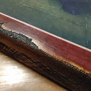 May include: Close-up of a wooden frame with a red and white border. The frame is chipped and worn, showing the wood underneath.