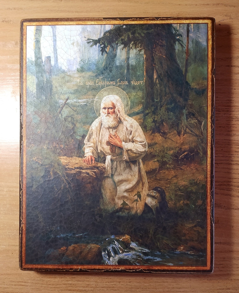 May include: A religious icon depicting a bearded man in a white robe kneeling in a forest setting. The icon is framed in a dark wood frame with gold accents. The text "Св. прп. Сергия Радонежского, моли Господи" is written in Cyrillic script at the top of the icon.