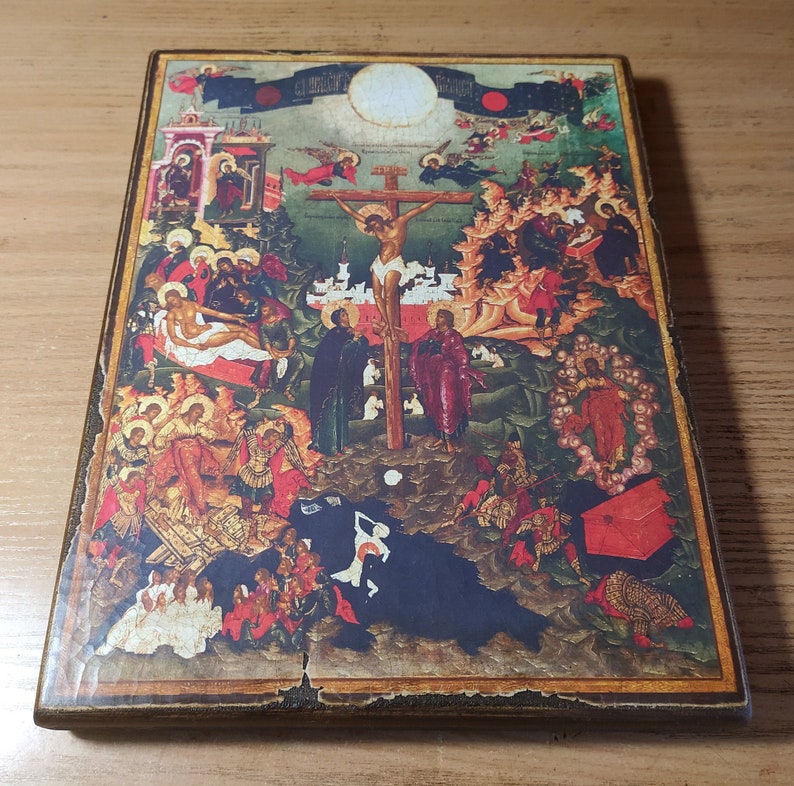 May include: A vintage religious icon featuring a detailed depiction of a crucifixion scene. The artwork showcases figures in various robes, with a central figure on a cross. The color palette includes reds, blues, and golds, with a distressed wooden frame.