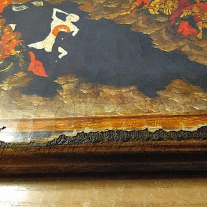 May include: Close-up of a section of a painting with a dark background and figures in red, gold, and white. The painting has visible cracks and damage along the edges, revealing the canvas and wooden frame.