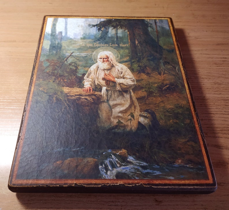 May include: A religious icon depicting a bearded man in a white robe kneeling in a forest setting. The icon is painted on a wooden panel and features a stream of water in the foreground. The text "Слава Господу Богу!" is written in Cyrillic script at the top of the icon.