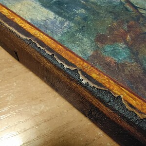 May include: Close-up of the edge of a wooden frame with a gold-colored border. The frame is slightly damaged, with some of the gold paint chipped away.