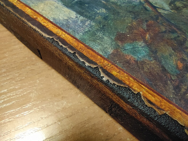 May include: Close-up of the edge of a wooden frame with a gold-colored border. The frame is slightly damaged, with some of the gold paint chipped away.