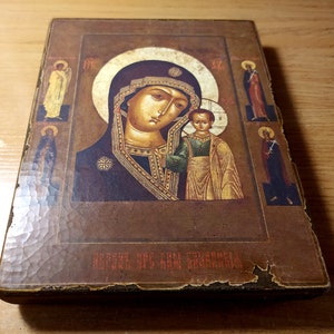 Puede incluir: Un icono de madera vintage que representa a la Virgen Mar&iacute;a y al ni&ntilde;o Jes&uacute;s. El icono est&aacute; pintado en un estilo tradicional con detalles dorados y tiene un fondo marr&oacute;n oscuro. El texto "БОЖИЯ МАТЬ" est&aacute; escrito en la parte inferior del icono.