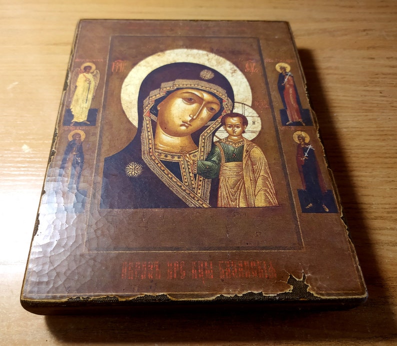 Puede incluir: Un icono de madera vintage que representa a la Virgen Mar&iacute;a y al ni&ntilde;o Jes&uacute;s. El icono est&aacute; pintado en un estilo tradicional con detalles dorados y tiene un fondo marr&oacute;n oscuro. El texto "БОЖИЯ МАТЬ" est&aacute; escrito en la parte inferior del icono.